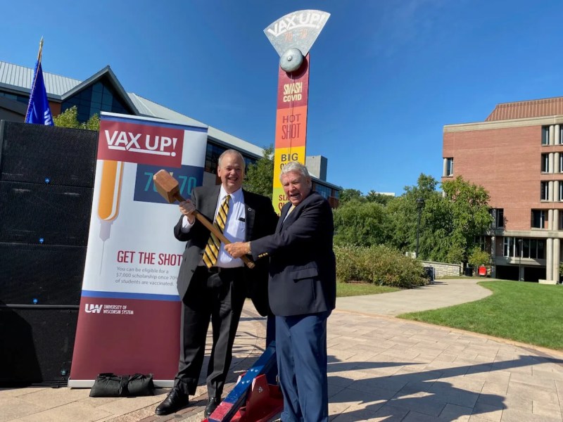 UW System Interim President Tommy Thompson, right, and UW-Eau Claire Chancellor James Schmidt pose after using a hammer to ring the bell on a “Smash COVID” carnival game during an event at the university Monday to promote students being vaccinated against the virus. (Photo by Julian Emerson)