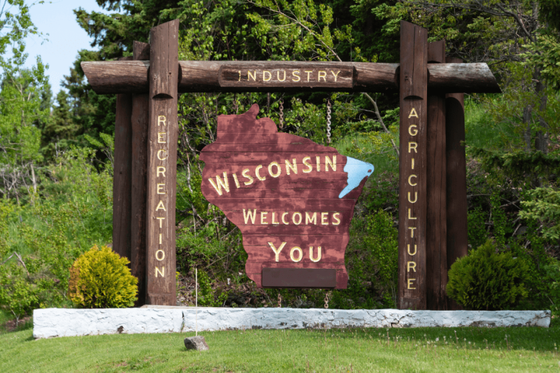 A wooden, Wisconsin-shaped sign post that says, "Wisconsin Welcomes You."