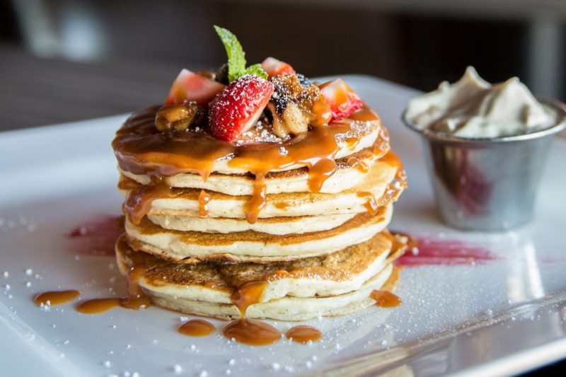 A stack of fluffy pancakes with fruit topping and a side of whipped butter.