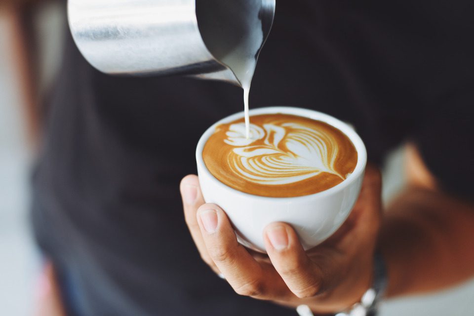 Someone pouring a foam leaf onto the top of a latte.