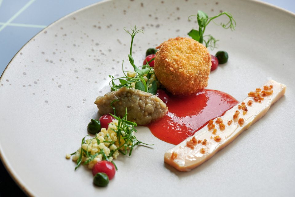 A plate with a fried item, herbs, and a red sauce.