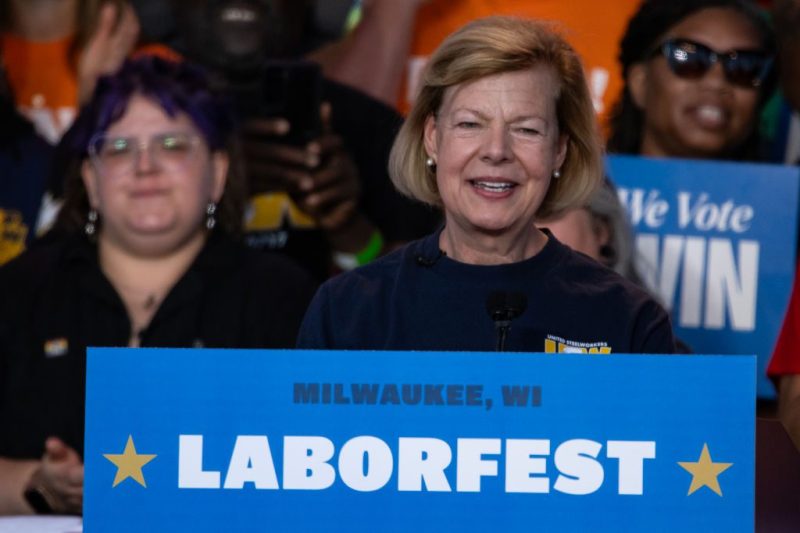Tammy Baldwin standing in front of a crowd. She is smiling behind podium, sign on podium reads "Labor Fest".