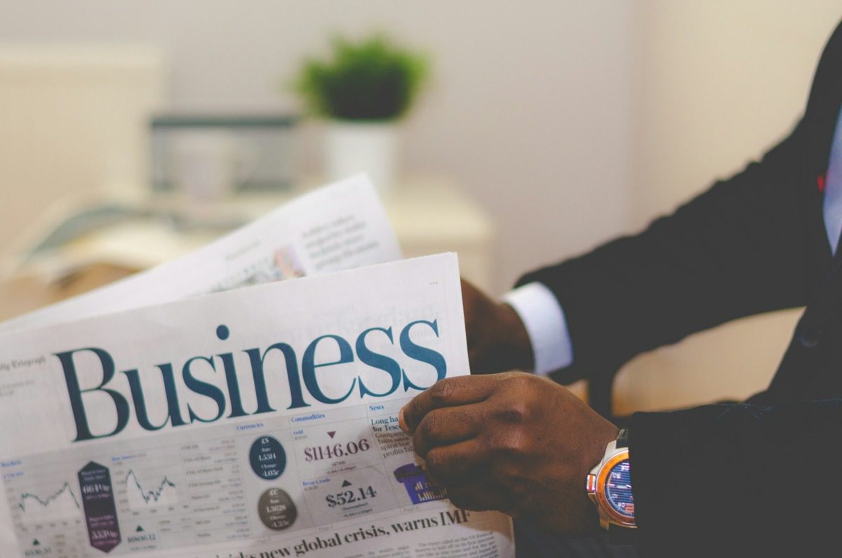 Black man's hands holding a newspaper that reads BUSINESS on the front.