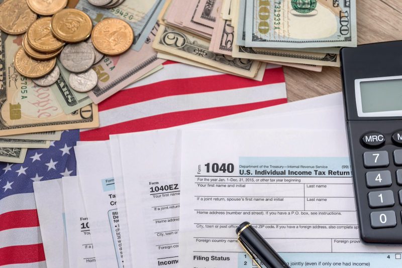 Tax forms, US currency, calculator, and a pen.