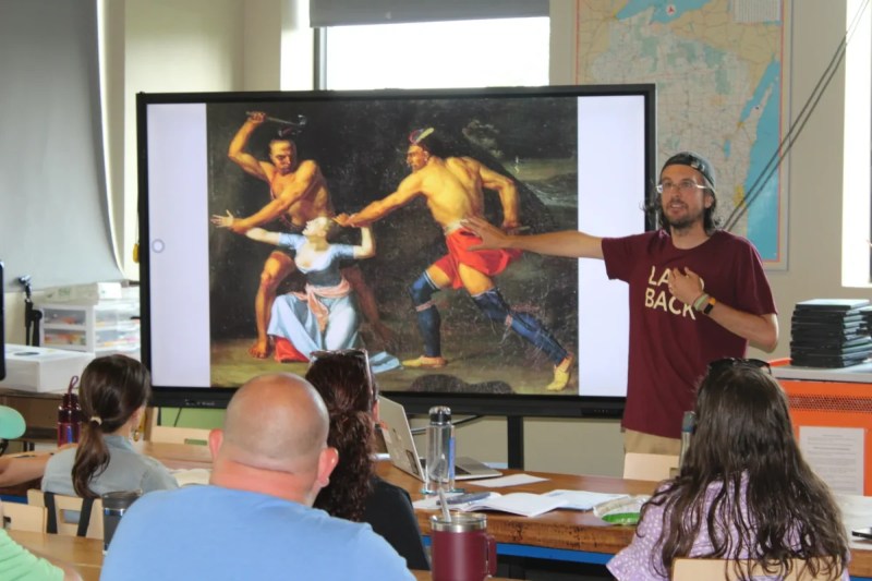 a man points to a piece of art in front of a classroom of people