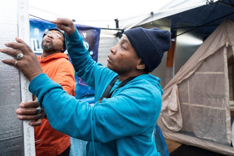 Economic Development co-chairs Jarvis West and Christal West attach a makeshift door to the bathroom area of a pop-up shelter to raise awareness of homelessness in Milwaukee.